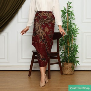 Op de afbeelding: Bordeaux wikkelrok met een batikpatroon met bruine en bruin-beige accenten. De rok is gedrapeerd en wordt gedragen met een witte blouse en nude hakken. De rok is knielang en heeft een uniek, asymmetrisch ontwerp.