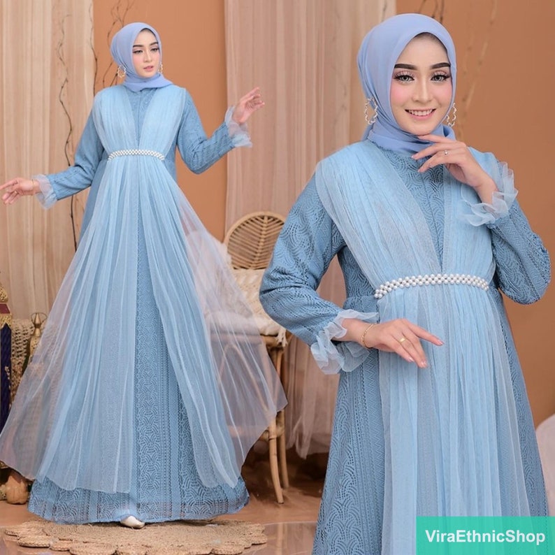 May include: A light blue maxi dress with a sheer overlay and a pearl-embellished belt. The dress has long sleeves and a V-neckline. The model is wearing a light blue headscarf.