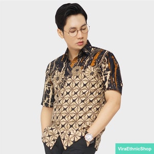 Può includere: Una camicia a maniche corte con un motivo batik nero e oro. La camicia ha un colletto abbottonato e un motivo floreale.