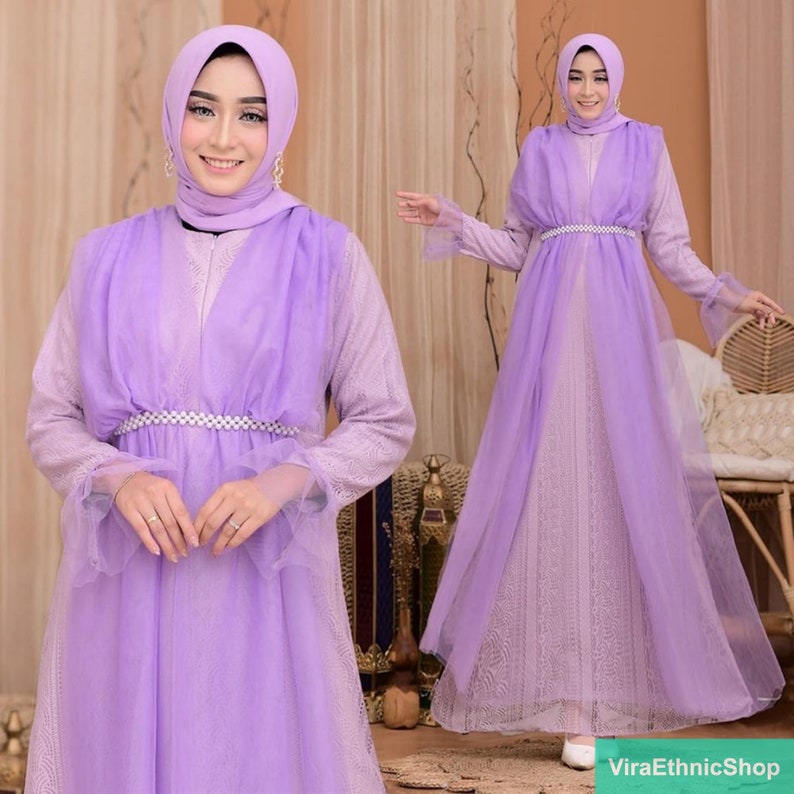 May include: A long, lilac-colored dress with a sheer overlay and a beaded belt. The dress has long sleeves with lace detailing and a flowing skirt.