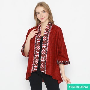 Op de afbeelding: Een rode kimono met een wit en bruin geometrisch patroon op de voorkant en mouwen. De kimono heeft een V-hals en is open aan de voorkant.