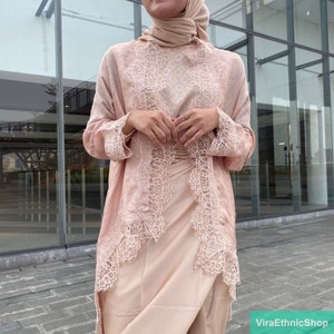 May include: A long-sleeved, blush-colored top with a lace trim. The top is made of a soft, flowing fabric and has a relaxed fit. The lace trim is delicate and adds a touch of elegance to the top.