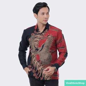 May include: A red and black long-sleeved shirt with a batik pattern featuring a golden eagle design. The shirt has a button-up collar and a button closure.