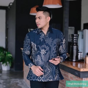 May include: A navy blue button-down shirt with a detailed floral and bird pattern. The shirt features long sleeves and a classic collar. The text "ViraEthnicShop" is visible in the bottom right corner.