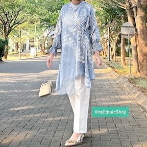 May include: A blue and white patterned tunic with a long sleeve and a tie at the waist. The tunic is worn with white pants and gold shoes. The text "ViraEthnicShop" is visible in the bottom right corner of the image.