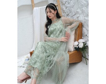 Puede incluir: Un vestido maxi verde claro con una superposición transparente y un delicado bordado floral. El vestido tiene un escote redondo y mangas largas con un detalle de volantes en los puños.