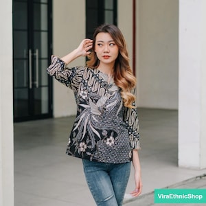 Peut inclure: Un chemisier à motifs noir et blanc avec un motif floral. Le chemisier a un col rond et des manches trois quarts. Le mannequin porte un jean bleu.