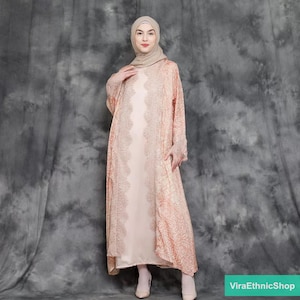 Puede incluir: Un vestido largo y fluido de color melocotón con una superposición de encaje y un pañuelo a juego. El vestido tiene un estampado floral y una falda larga y fluida.