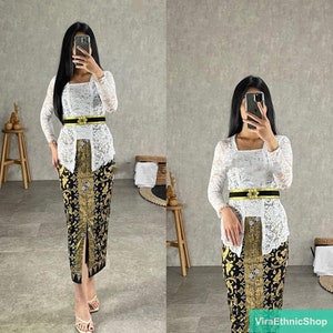 May include: A white lace top with long sleeves and a black belt with gold accents. The top is paired with a black and gold patterned skirt.