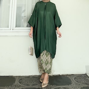 Op de afbeelding: Een loszittende, donkergroene top met lange mouwen en een hoge halslijn en een geruite rok. De rok is beige met groene bloemenpatronen.