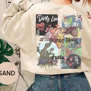 May include: Sand-colored sweatshirt with a multi-panel graphic design. The design includes the words "Dirty Love," "MT. JOY," "Orange Blood," "Julia," and "Silver Lining." The phrase "hope we have fun" is also printed on the sweatshirt.