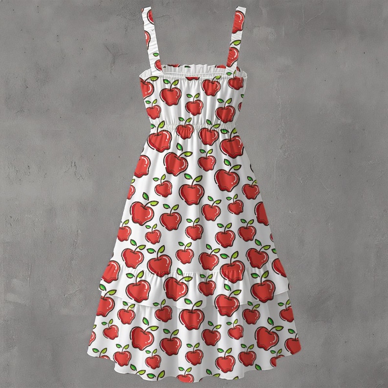 May include: White sundress with red apple pattern. The dress features a square neckline, thin straps, and a tiered skirt. The apples have green leaves and stems. The dress is made of a lightweight fabric.