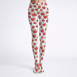 May include: White leggings with a repeating pattern of red apples. Each apple has a green stem and leaf. The leggings are made of a stretchy material and are suitable for casual wear.