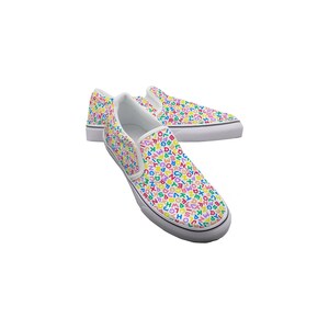May include: A pair of white slip-on sneakers with a colorful alphabet pattern. The shoes have a white sole and a white interior. The letters are in various colors, including red, blue, green, and yellow. The shoes are casual and stylish.