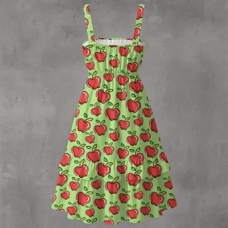 May include: A green sundress with a red apple pattern. The dress has a tiered skirt, spaghetti straps, and a white ruffled neckline. The apples have green leaves and stems.