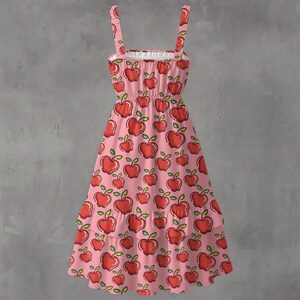 May include: A pink sundress with a repeating pattern of red apples with green leaves. The dress has thin straps, a ruffled neckline, and a tiered skirt. The dress is made of a lightweight fabric.