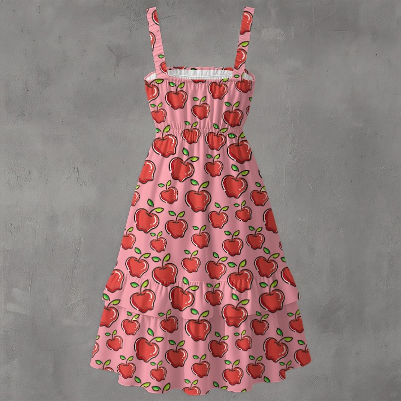 May include: A pink sundress with a repeating pattern of red apples with green leaves. The dress has thin straps, a ruffled neckline, and a tiered skirt. The dress is made of a lightweight fabric.