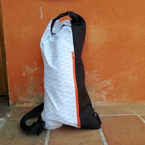 Könnte beinhalten: Eine weiße und schwarze Kordeltasche mit einem leuchtend orangefarbenen Reißverschluss. Die Tasche hat ein Rautenmuster auf der Vorderseite und einen schwarzen Riemen.