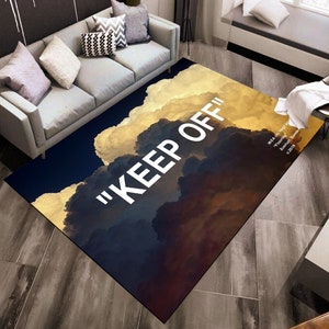 Può includere: Un tappeto nero e oro con un design a nuvole e il testo "KEEP OFF" in bianco. Il tappeto è in un soggiorno con un divano e una sedia.