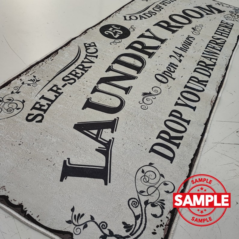 May include: A white sign with black text that reads "Self-Service 25 Loads of Laundry Room Open 24 Hours Drop Your Drawers Here". The sign has a distressed look and features decorative floral designs.