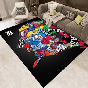 May include: A black and white rug featuring a map of the United States of America. The map is made up of logos from different NBA teams, including the Spurs, Celtics, Lakers, and Knicks. The rug has the word "NBA" in white letters at the top.