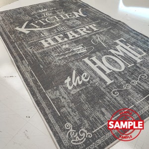 May include: A gray and white kitchen rug with the text "The Kitchen is the Heart of the Home" in a vintage style font. The rug has a distressed look and a white border.