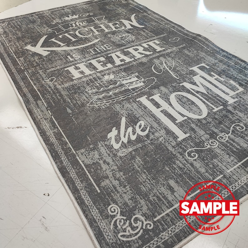 May include: A gray and white kitchen rug with the text "The Kitchen is the Heart of the Home" in a vintage style font. The rug has a distressed look and a white border.