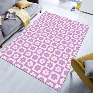 May include: A rectangular area rug with a repeating pattern of pink and purple flowers in a checkerboard design. The rug is primarily pink and purple, with a light pink background and a darker purple for the squares.