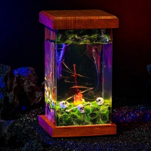 May include: A wooden box with a glass front containing a miniature scene of a sword stuck in the ground with a small fire and skulls around it. The scene is set on a bed of green moss.