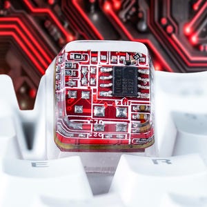 May include: A red circuit board encased in clear resin, sitting on a white keyboard. The circuit board has a black integrated circuit chip with the text "LM358" and "ST227" printed on it.