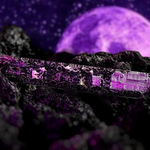 Könnte beinhalten: Ein durchsichtiger Glas-Briefbeschwerer mit einem detaillierten 3D-Design einer Lokomotive. Der Briefbeschwerer liegt auf einer dunklen, felsigen Oberfläche mit einem violetten Mond im Hintergrund.