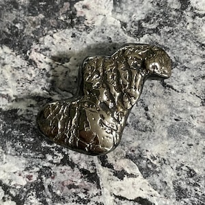 May include: A dark, metallic-looking sculpture with an abstract shape. The object has a textured surface and a reflective sheen, suggesting it is made of metal. The sculpture is set against a mottled gray and white background.
