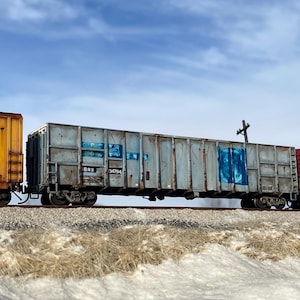 May include: A weathered, gray train car with blue graffiti and the text "BRX 34794" on the side. The car is part of a train with a yellow car in the front and a red car in the back.