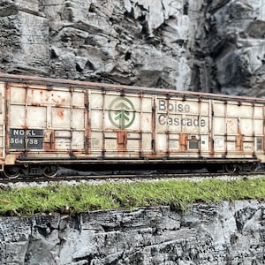 May include: A weathered white boxcar with the words "Boise Cascade" and a green tree logo. The car is labelled "NOKL 504 738".