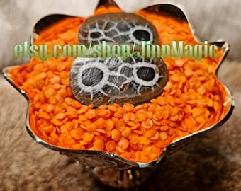 May include: A silver-colored, star-shaped bowl filled with orange lentils, holding two oval-shaped stones. The stones have a dark brown and gray pattern with white and black circular designs. The text "etsy.com/shop/linnMagic" is visible.