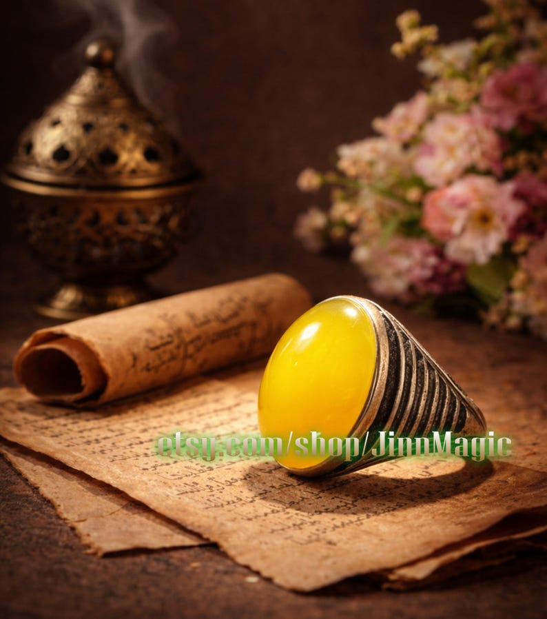 May include: A silver ring with a large, oval, yellow gemstone. The ring is set against a backdrop of aged paper, a rolled scroll, and a decorative metal incense burner. The Etsy shop name "JinnMagic" is visible on the paper.