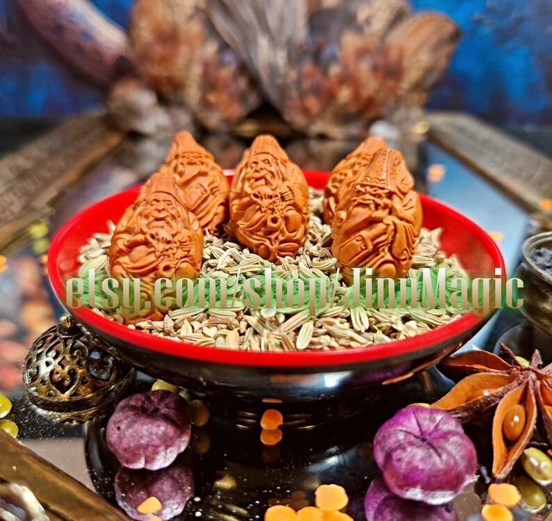 May include: A red and black bowl filled with brown carved figurines and seeds. The figurines are in the shape of a bearded man. The bowl is surrounded by star anise, purple berries, and other decorative items. The text "etsy.com/shop/TinyMagic" is visible.