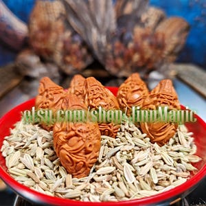 May include: A red bowl containing fennel seeds and several small, intricately carved wooden figures. The brown figures appear to be carved with faces. The text "etsy.com/shop/linnMagic" is visible on the bowl.