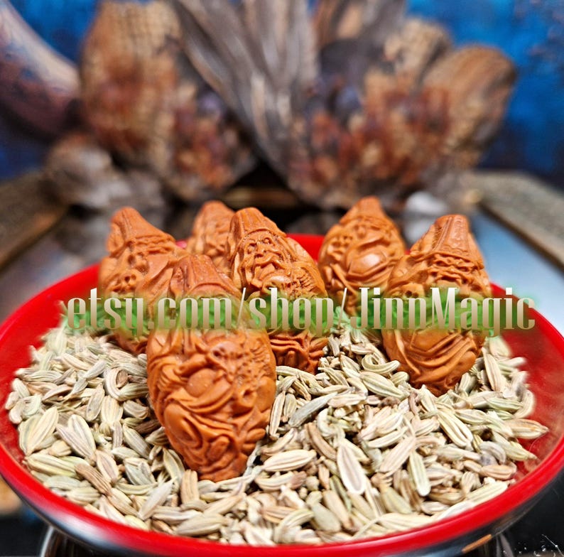 May include: A red bowl containing fennel seeds and several small, intricately carved wooden figures. The brown figures appear to be carved with faces. The text "etsy.com/shop/linnMagic" is visible on the bowl.