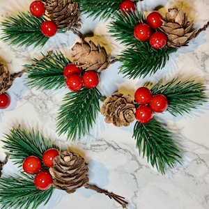 May include: A close-up of Christmas decorations featuring faux pine branches, red berries, and brown pine cones. The arrangement is set against a white and grey marbled background, creating a festive holiday theme.