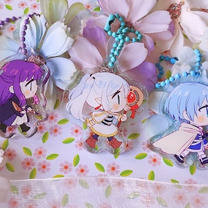 May include: Four colourful anime character keychains with glitter accents. Each keychain features a different character with unique clothing and accessories. The keychains are made of clear acrylic and have a silver chain.