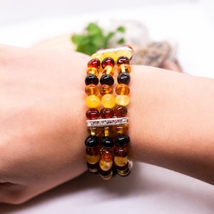 May include: Multi-strand amber bracelet with a silver spacer bar set with clear rhinestones. The bracelet features a mix of amber beads in shades of yellow, orange, and brown.