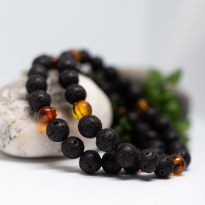 Peut inclure: Un bracelet en perles de lave noire et d'ambre. Le bracelet est composé de petites perles rondes et est présenté sur une surface blanche.