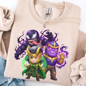 May include: Beige crewneck sweatshirt featuring a colorful graphic of Venom, Loki, and Thanos in a cartoon style. The characters are depicted with exaggerated features and surrounded by swirling purple and green energy.