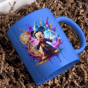 May include: A blue ceramic mug with a colourful illustration of Mickey Mouse as a wizard. The design includes a wizard's hat, staff, and magical symbols. The mug is set against a background of brown packing material.