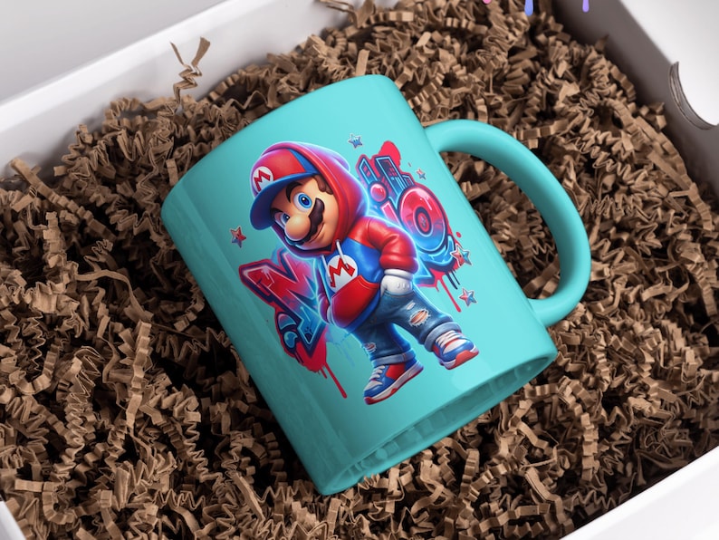 May include: A teal ceramic mug featuring a cartoon illustration of a character in a red hoodie and blue jeans. The design includes graffiti-style lettering and stars. The mug is presented in a white box with brown paper filler.