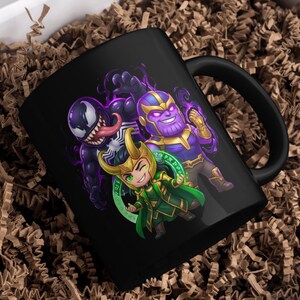 May include: Black ceramic mug featuring cartoon illustrations of Venom, Thanos, and Loki. The characters are depicted in vibrant colors against a black background. The mug is placed in a white box with brown packing material.