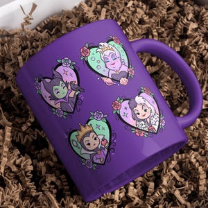 May include: A purple ceramic mug featuring four heart-shaped illustrations of Disney villains. Each heart has a different villain, surrounded by floral and decorative elements. The mug is in a gift box with brown paper filler.