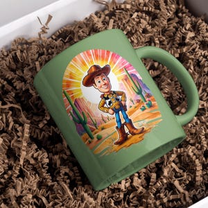 May include: A green ceramic mug with a cartoon image of Woody from Toy Story. Woody is standing in a desert landscape with a sunset behind him. The mug has a handle on the right side.