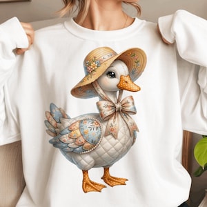 Può includere: Felpa bianca con un'illustrazione di un'oca dei cartoni animati. L'oca indossa un cappello di paglia con dettagli floreali e un fiocco. L'oca ha un corpo trapuntato con motivi pastello e floreali. Un design stravagante e dettagliato.